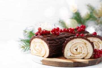 Delicious Yule log (traditional Christmas cake) with redcurrant on white tiled table, closeup. Space for text