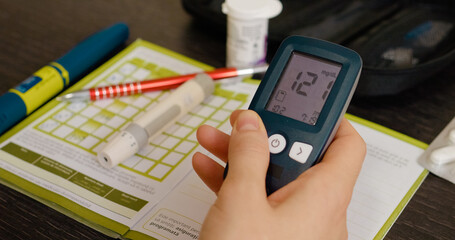 A woman closely examines her blood sugar test history in a glucometer diary, reflecting on her glucose levels to manage her diabetes effectively.
