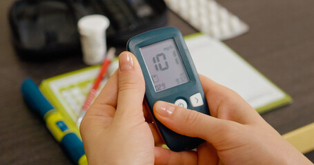 A woman examines her blood sugar test history in a glucometer diary, focusing on her glucose levels to manage diabetes and monitor health effectively.
