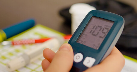 Woman is reviewing her blood sugar test results in a glucometer diary, tracking her glucose levels to manage her diabetes and maintain health.
