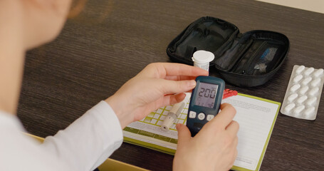 A woman measures her blood sugar levels using a glucometer, revealing elevated glucose readings in her home as she manages her diabetes condition.