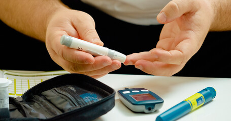 Man pricks his finger to draw blood using a glucometer in a home setting. He carefully handles the...
