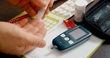 A man prepares to prick his finger with a lancet for a blood sugar test while monitoring his glucose level at home. He evaluates his health status carefully.