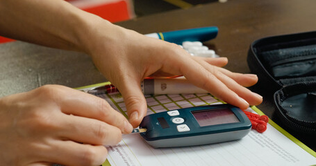 A woman carefully inserts a test strip into a glucometer to check her blood sugar levels, a crucial...