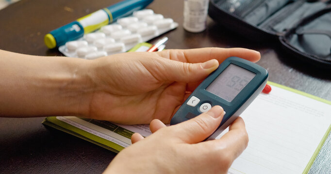 A woman anxiously examines her blood glucose meter result, revealing levels that fall between normal and prediabetes. She hopes for a good outcome as she tests. - Powered by Adobe