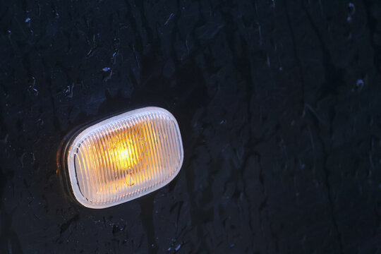 Close up of glowing amber turn signal light. An automotive indicator lamp on vehicle dark metal panel, warm warning signal for transportation safety and direction