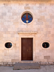 front entrance to St. Roko Church with old brown timber door and round windows against stone wall located in Bibinje, Croatia 