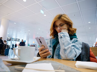 Bored woman passenger typing on phone at the airport. Woman uses smartphone in the airport lounge...