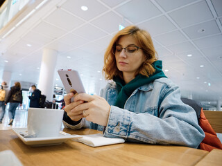 Freelancer working on the smartphone in the airport lounge while waiting the flight. Woman passenger uses phone and while sitting at departure lounge.