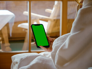 Woman isolated in her chalet room with green screen phone in her hands. Young female addiction to gadgets watching chroma key screen in a Hotel Room. Travel, tourism and technology concept.
