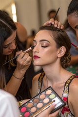 Many hands applying makeup on woman's face on blurred background