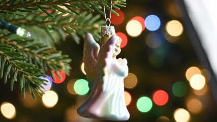 Delicate angel ornament praying on Christmas tree branch. Festive holiday decoration with colorful bokeh lights background - Powered by Adobe