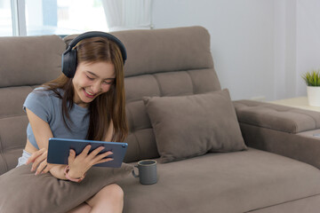 Young happy woman enjoys home activity, people find joy using digital tablet, wearing headphones, relaxing on comfortable living room sofa with entertainment, leisure time