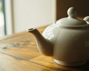 Elegant ceramic teapot resting on a warm wooden table bathed in soft natural light, creating a serene and inviting atmosphere for tea time.