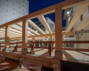 Modern building construction site of a sustainable Timber-concrete composite office building at night with exposed timber beams and structural framework illuminated by artificial light