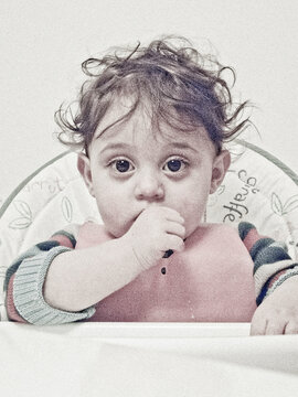A baby in a high chair with a bib, sucking on their fingers.