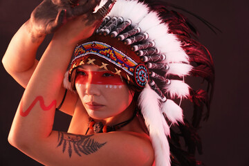 Shaman woman in native American Indian headdress with face painting on dark background