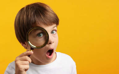Surprised little boy with magnifying glass on yellow background. Space for text