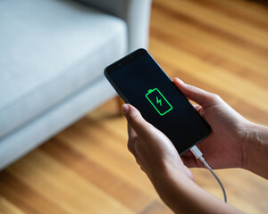 Close-up of hands plugging charging cable into smartphone displaying vibrant green battery icon with lightning bolt symbol