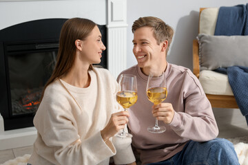 Lovely couple with glasses of wine near fireplace indoors