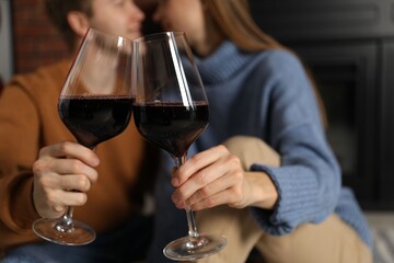 Lovely couple with glasses of wine near fireplace indoors, selective focus