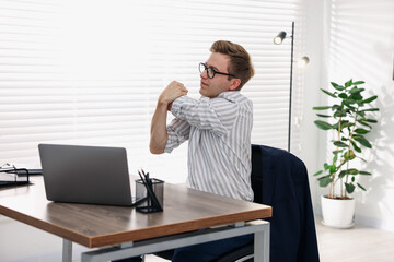 Young businessman stretching his arm at table in office