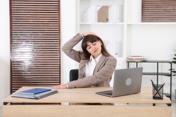 Young businesswoman stretching her neck at table in office