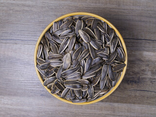 Striped sunflower seeds in a bowl on a wooden table.