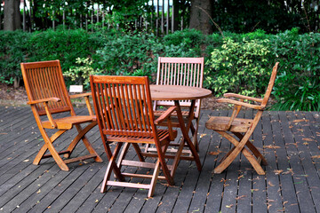 Obraz premium 新緑に囲まれたウッドデッキのガーデンファニチャー：木製テーブルと椅子のあるテラスの休憩空間。アウトドアリビング、リゾート、カフェ、自然の中でのリラックスタイムを伝えるイメージ素材。