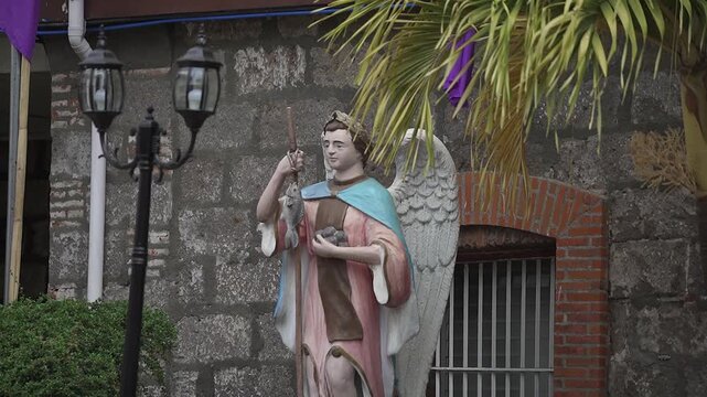 Statue of Archangel Raphael holding a fish and staff outside an old stone church in San Rafael, Bulacan, Philippines &mdash; symbol of healing, guidance, and divine protection in Catholic tradition.