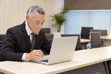 Serious Asian senior businessman in suit typing on laptop at working desk. Elderly successful male boss work on laptop computer at office workplace. Asian mature man business worker with technology.