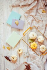 A cozy fall flat lay with mini pumpkins, books, and a gold tray in pastel colors. Autumn still life: pumpkins, leaves and books on a rustic surface, top view.