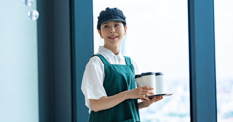 コーヒーカップを持つエプロンをつけた女性カフェスタッフ