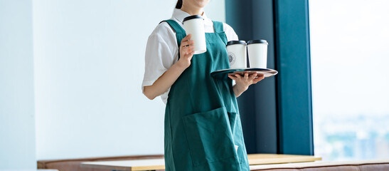 コーヒーカップを持つエプロンをつけた女性カフェスタッフ