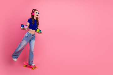 Young woman roller skating on pink background holding colorful beverages, wearing trendy outfit and smiling confidently