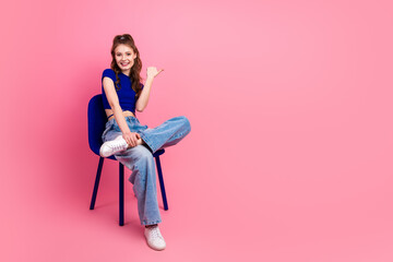 Stylish young woman sitting casually, wearing trendy blue top and jeans against vibrant pink...