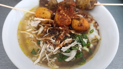 Delicious Indonesian chicken porridge or bubur ayam topped with fried shallots, soy sauce, and sliced chicken, served in a traditional bowl.