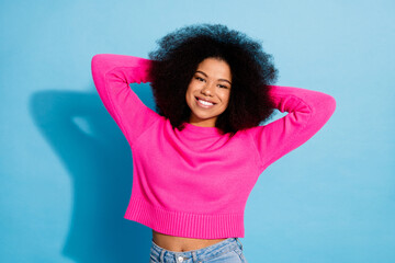 Stylish young woman in vibrant pink outfit posing confidently with hands behind head on a bright...