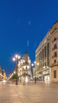 Avenida de la Constitucion day to night timelapse in Seville, Spain. Historic architecture with modern streetlights, pedestrians and urban atmosphere. Iconic Adriatica building glowing after sunset.