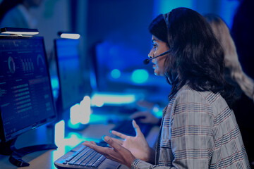 Focused female professional works diligently late night modern tech office analyzing data screen headset communication active intense concentration achieve project goals now vibe.