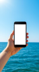 Hand holding smartphone with blank white screen against blue ocean and sky mobile phone cell phone