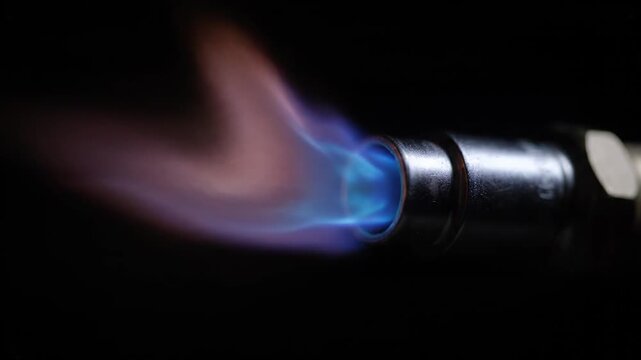 Macro shot of a butane or propane gas torch nozzle igniting, producing a vibrant blue and orange flame, burning vigorously, and then being put out