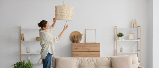 Young woman screwing light bulb into stylish lamp in living room