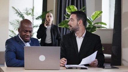 Group of three professionals engaged in a business meeting, discussing documents and strategies, surrounded by greenery in a modern office environment, showcasing collaboration and teamwork - Powered by Adobe