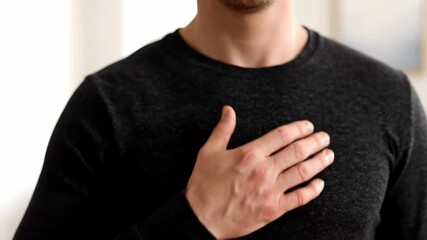 Unidentified person wearing a black shirt, holding a pink ribbon the emblem of breast cancer awareness month, with one hand on their chest