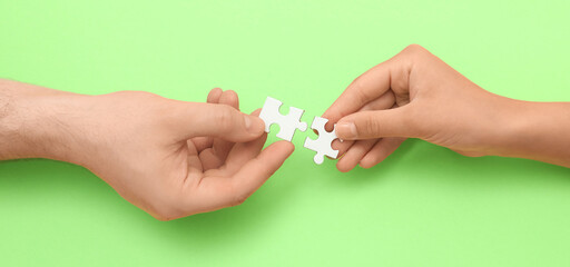 Hands of loving young couple with puzzle pieces on green background