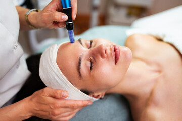 Professional beautician using a plasma pen device, performing a non-surgical skin tightening...