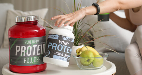 Sporty young woman with jars of protein powder, fruits and shake sitting on sofa at home, closeup