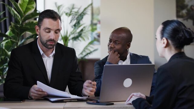 Two professional men engaged in a collaborative discussion while working on a laptop at a modern office space, showcasing teamwork and innovation in a business environment	