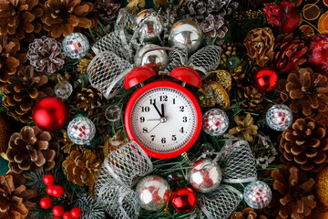 The bright red alarm clock shows five minutes to midnight. A New Year's composition with cones and...